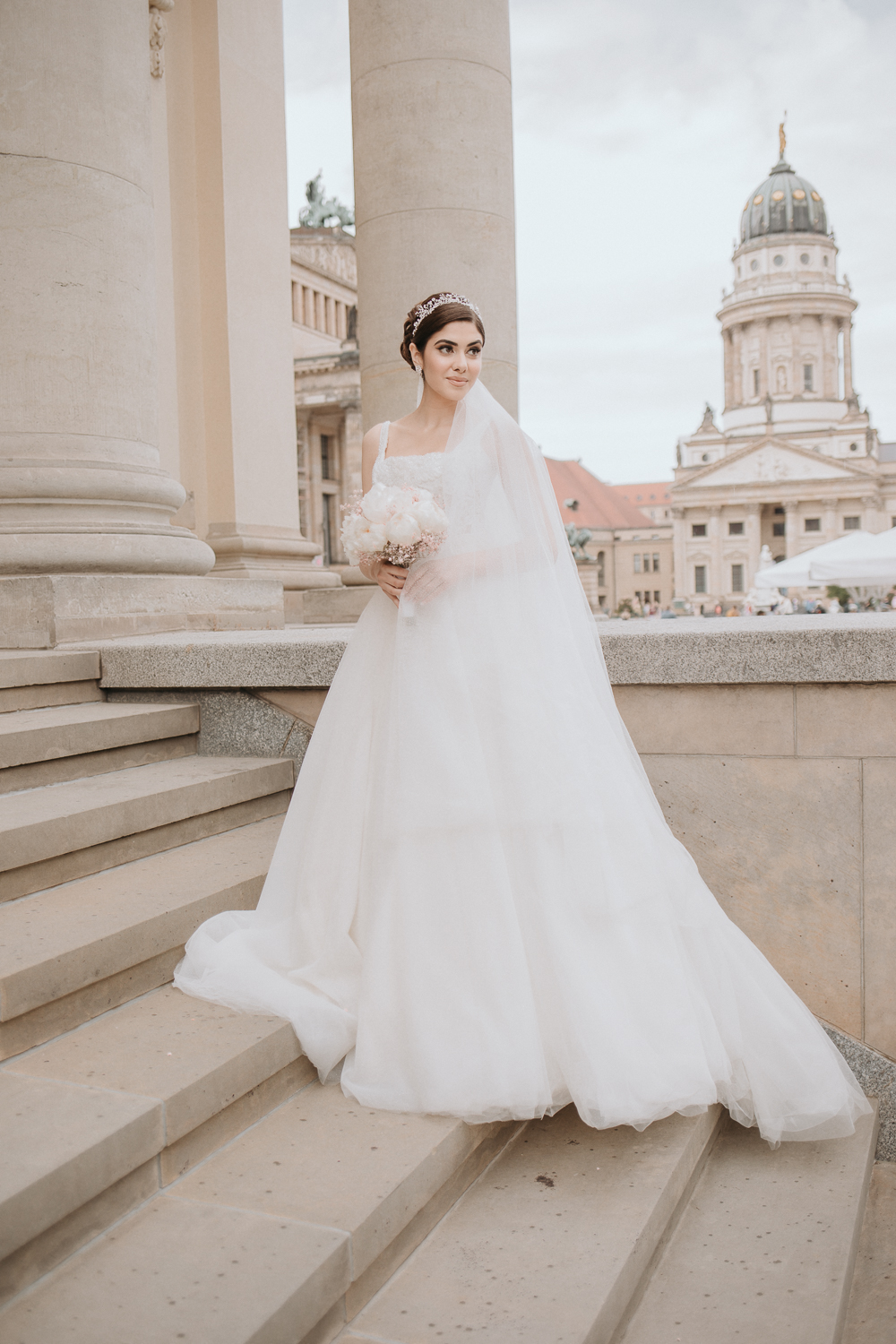 Die Braut steht alleine vor dem Konzerthaus und schaut nicht direkt in die Kamera. Das wundersche Brautkleid ist vollst