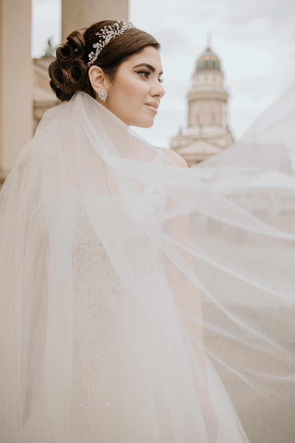 Nochmal ein eher untypisches Foto der Braut. Diesmal eher im Portraitformat. Man sieht lediglich ihr Gesicht und ein Teil des Brautschleiers. Im Hintergrund ist das Konzerthaus zu erkennen. Sie schaut an mir vorbei, in Richtung Stra